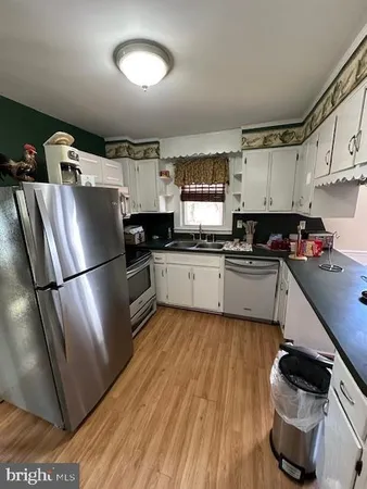a kitchen with granite countertop a refrigerator a sink dishwasher a stove top oven a dining table and chairs with wooden floor