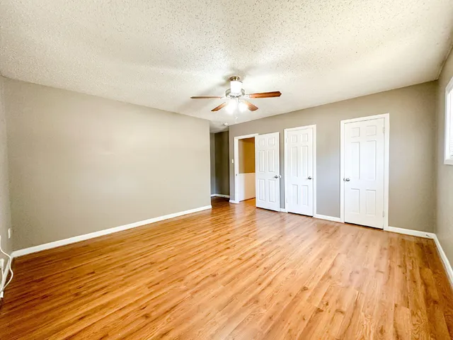 a view of an empty room with wooden floor and a ceiling fan