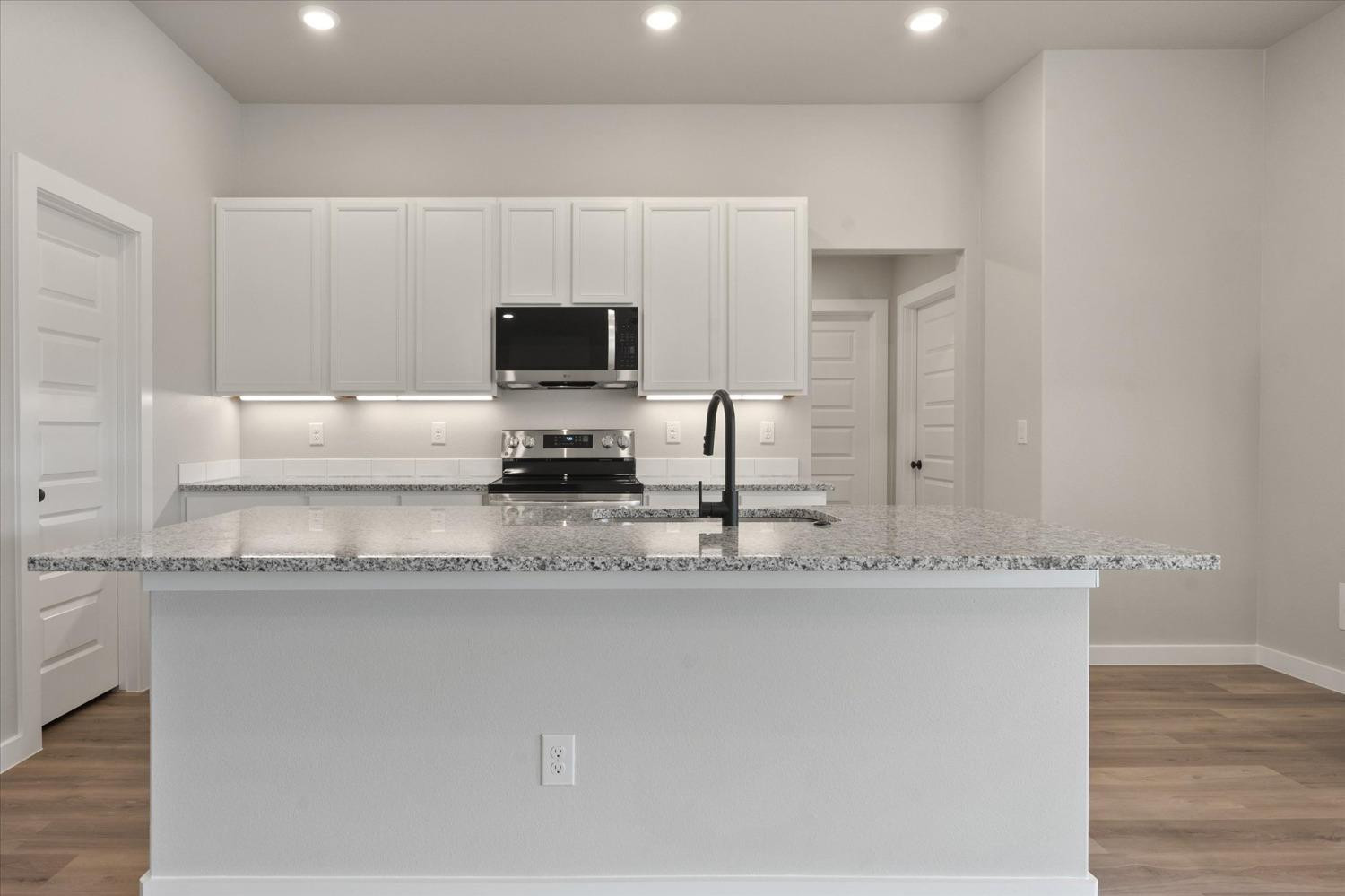 7429 30th Street Lubbock, TX 79407 - Photo 8 of 20 a kitchen with granite countertop a sink a stove a microwave and wooden cabinets
