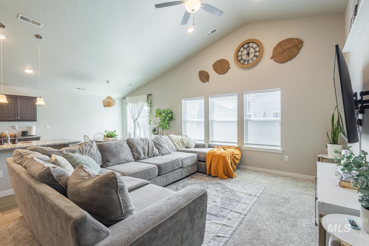 12623 Shadow Peak Street Caldwell, ID 83607 - Photo 12 of 50 Open-concept living area featuring a vaulted ceiling with a ceiling fan, three large windows with blinds, and light gray carpeting