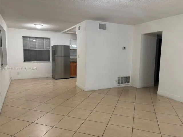 a view of a refrigerator in kitchen and empty room with windows