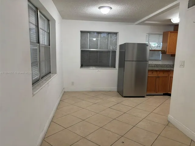 a view of a refrigerator in kitchen and an empty room and wooden floor