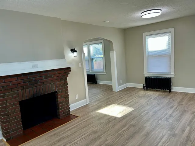 an empty room with wooden floor fireplace and windows