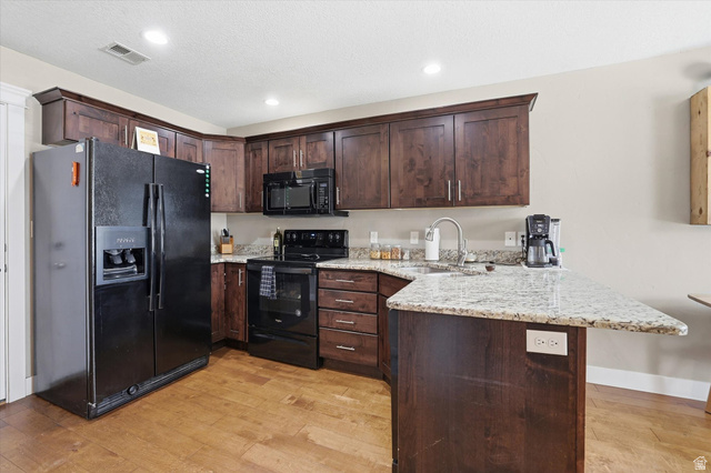 1024 South 270 West Logan, UT 84321 - Photo 11 of 37 Kitchen featuring dark wood finish cabinets, a peninsula, black appliances, light stone countertops, and light wood-style floors
