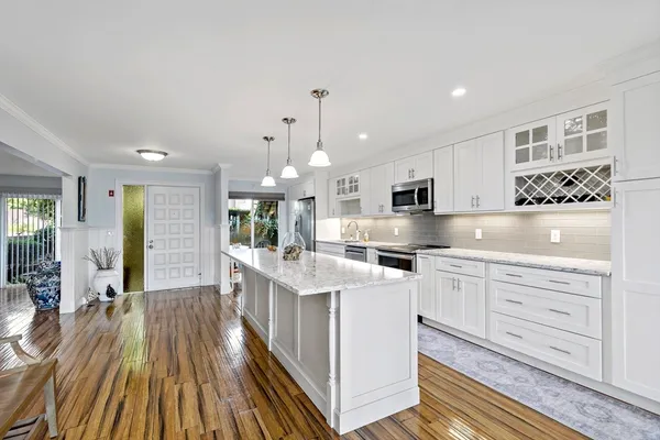 a large white kitchen with kitchen island a stove a sink dishwasher and white cabinets with wooden floor