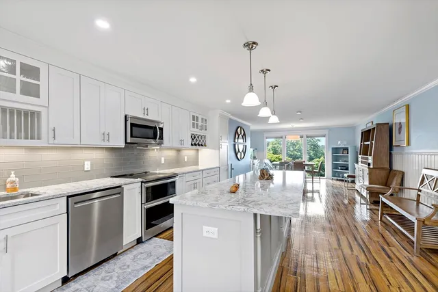 a kitchen with stainless steel appliances granite countertop a stove top oven a sink dishwasher and white cabinets with wooden floor