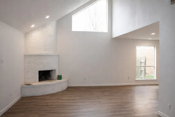 an empty room with wooden floor fireplace and windows
