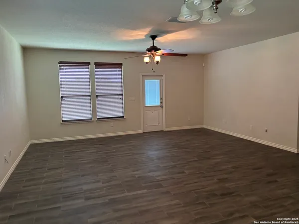 an empty room with wooden floor chandelier fan and windows