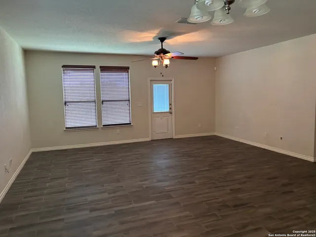 an empty room with wooden floor chandelier fan and windows