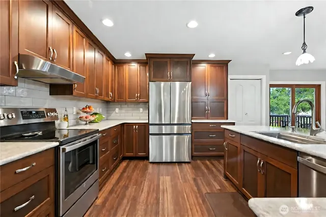 a kitchen with stainless steel appliances granite countertop wooden cabinets a refrigerator a sink a stove and wooden floors