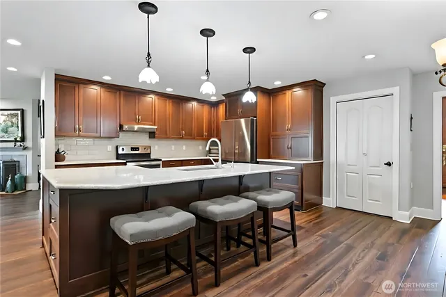 a kitchen with stainless steel appliances kitchen island granite countertop a table chairs sink and wooden floor