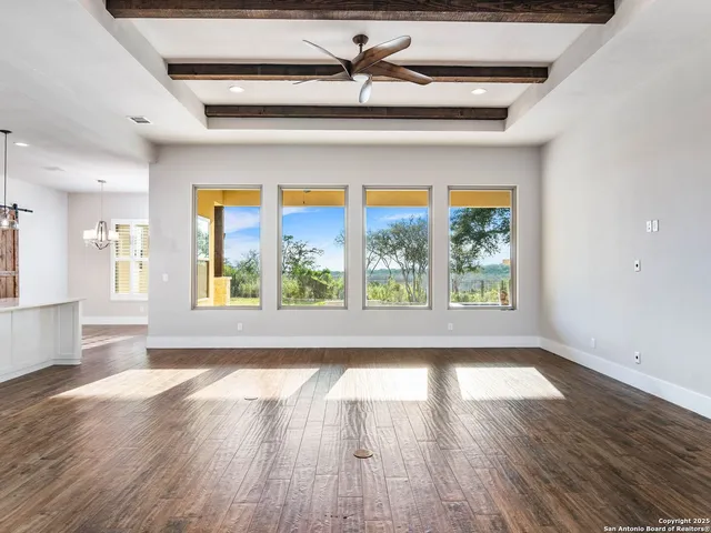 a view of an empty room with wooden floor and a ceiling fan