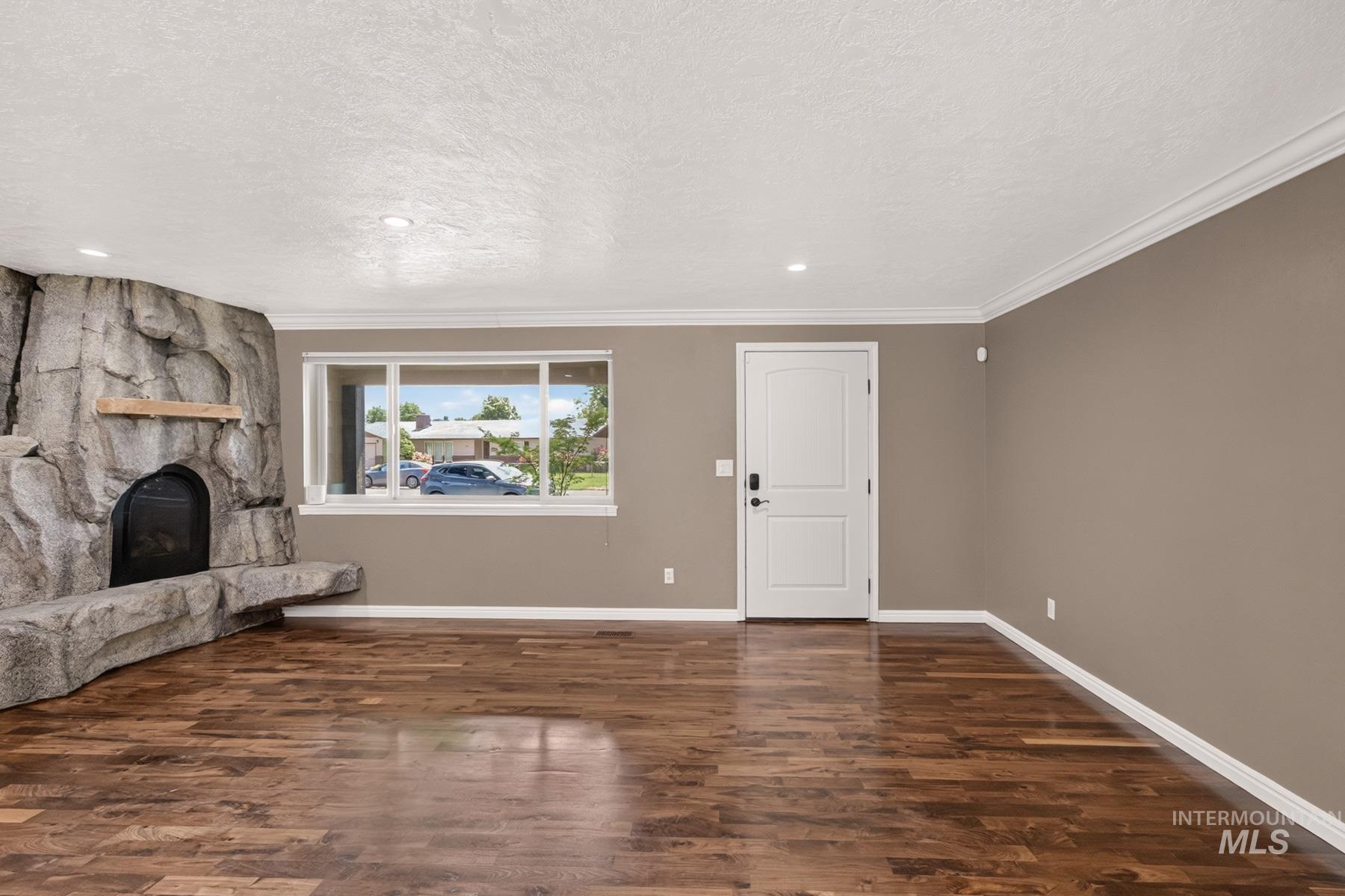 9622 Delaware Street Boise, ID 83709 - Photo 8 of 48 Spacious interior featuring wood-finish flooring, a prominent stone-clad fireplace with hearth, a large window, a paneled entry door, and crown molding