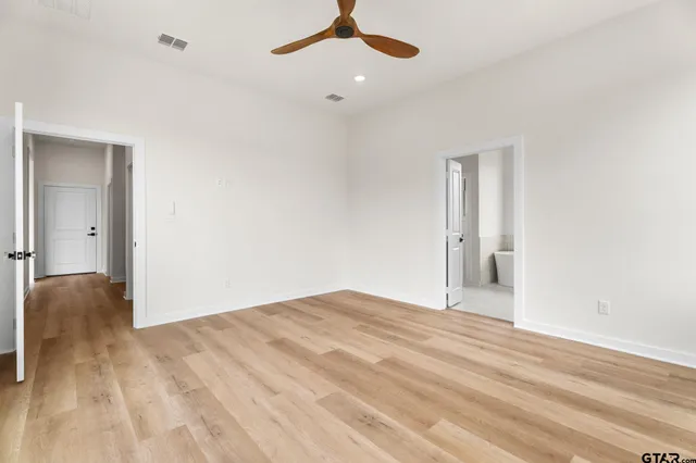 a view of an empty room with wooden floor and a ceiling fan
