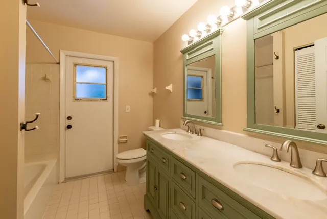 a bathroom with a granite countertop double vanity sink a mirror and a toilet