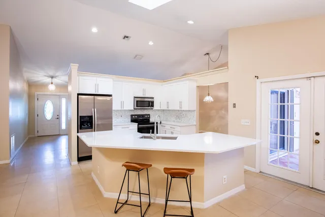 a dining hall with stainless steel appliances kitchen island granite countertop a refrigerator a stove top oven and a sink with wooden floor