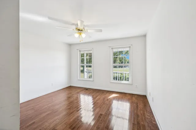 an empty room with wooden floor and a ceiling fan