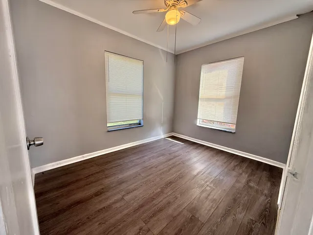 an empty room with wooden floor fan and windows