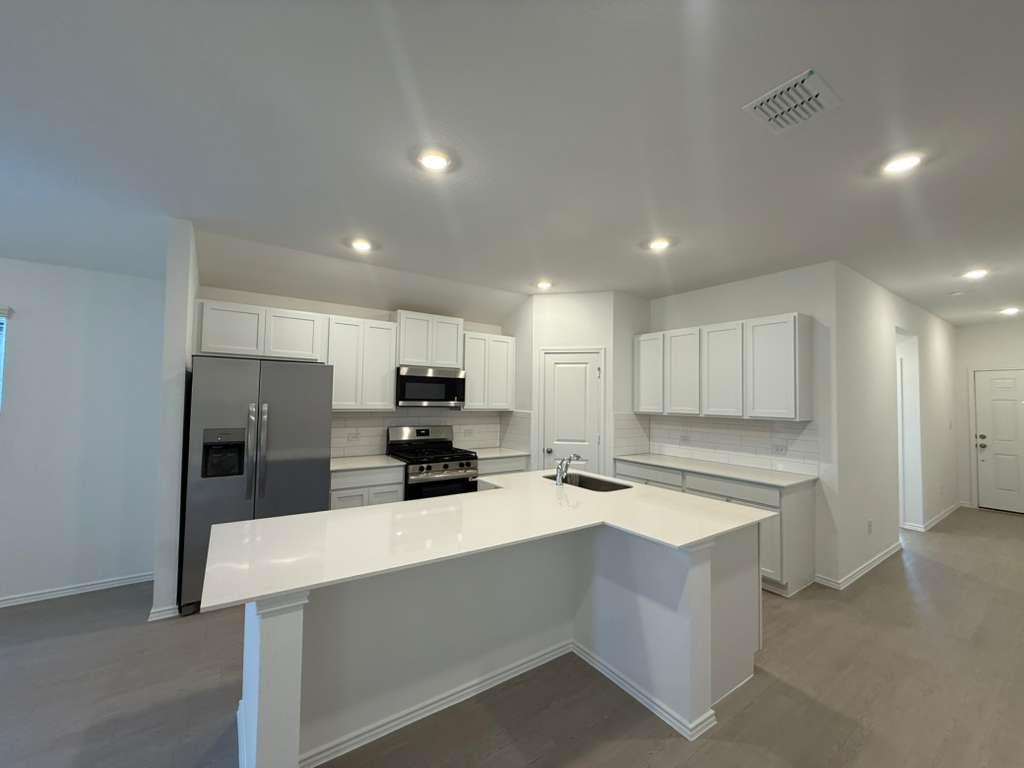 545 Sormonne Loop Kyle, TX 78640 - Photo 12 of 39 Kitchen with decorative backsplash, stainless steel appliances, white cabinets, a center island with sink, and recessed lighting