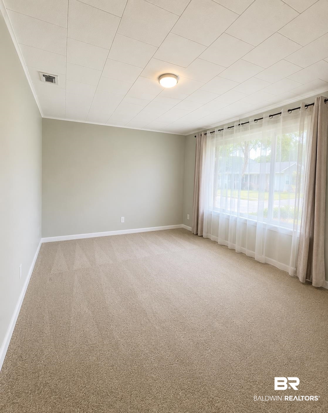 226 Elizabeth Street Evergreen, AL 36401 - Photo 16 of 35 Spacious room featuring neutral wall paint, light-colored carpet, a large window with sheer and blackout curtains, and a flush-mount ceiling light fixture