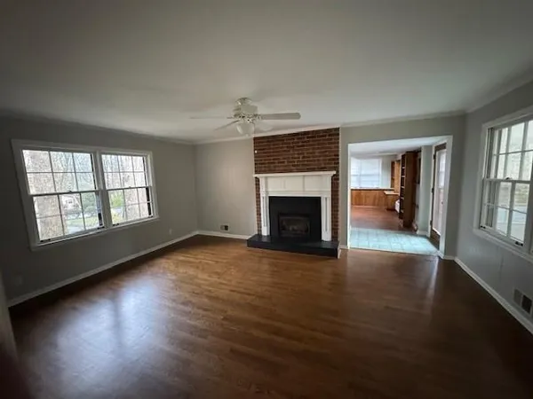 an empty room with wooden floor fireplace and windows