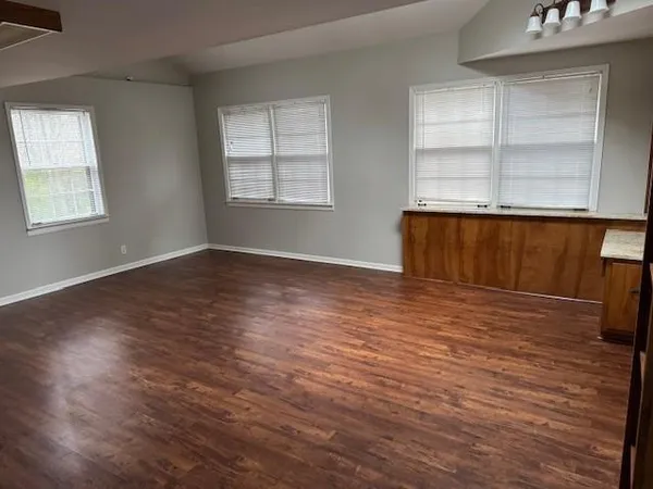 an empty room with wooden floor cabinet and windows