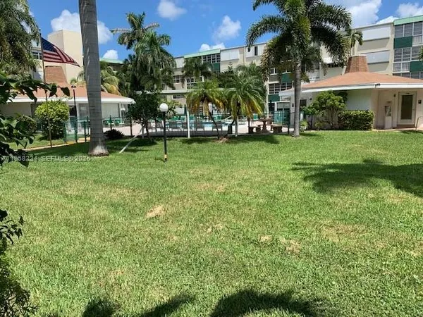 a view of a white house with a big yard and potted plants and palm trees