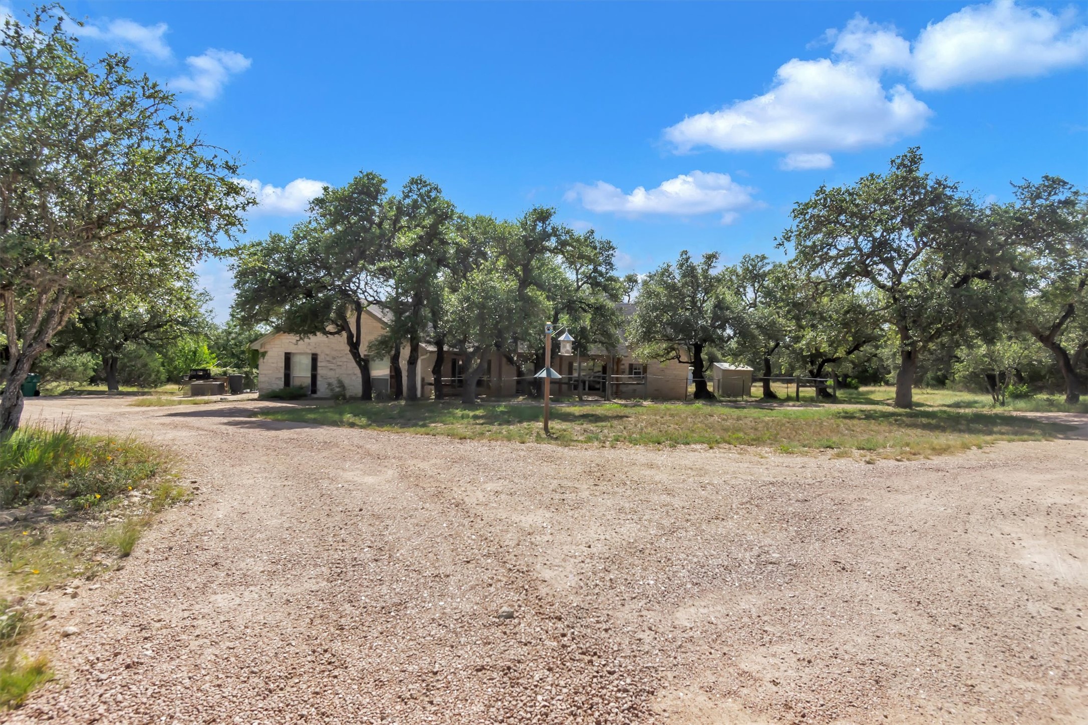 1120 Meadow Ridge Drive Austin, TX 78737 - Photo 4 of 40 A private gravel driveway leads to a secluded residence nestled amongst mature trees, offering ample parking and a tranquil setting.