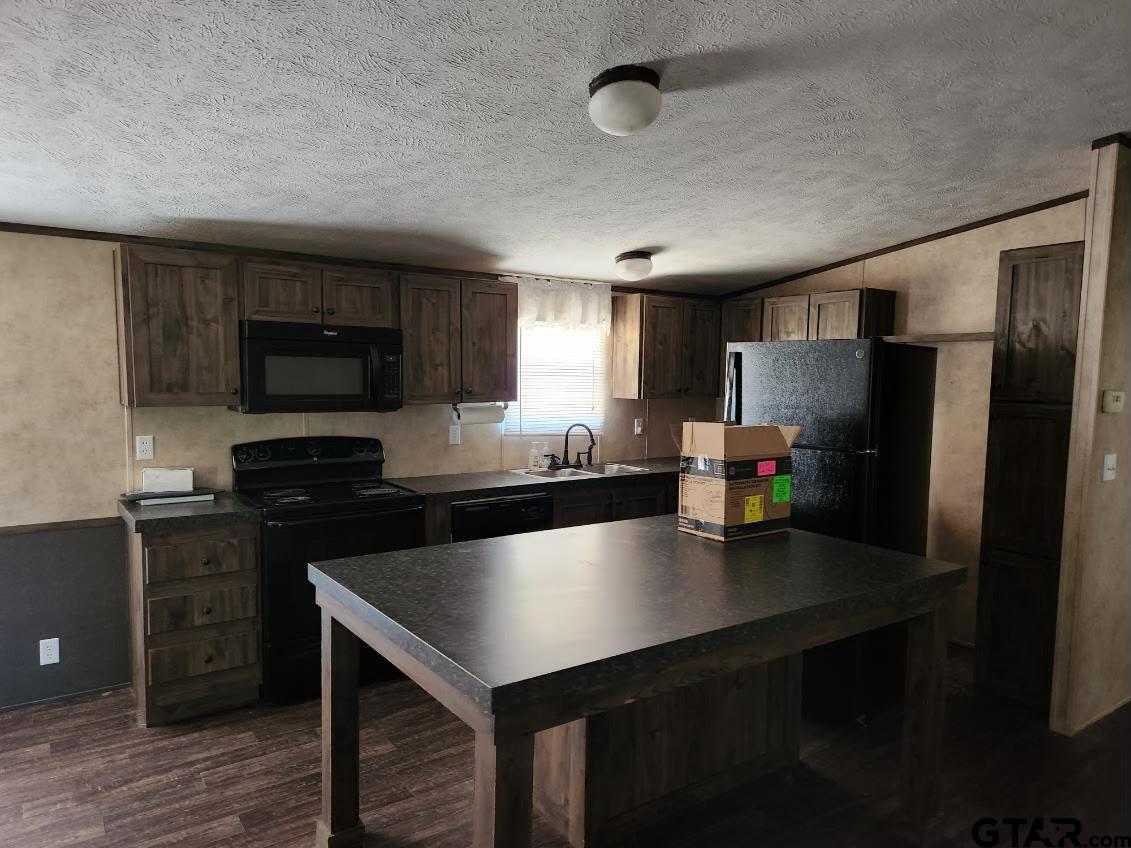 6339 Gorilla Road Gilmer, TX 75644 - Photo 7 of 12 a kitchen with stainless steel appliances a sink dishwasher a refrigerator a stove top oven and a center island with wooden floor