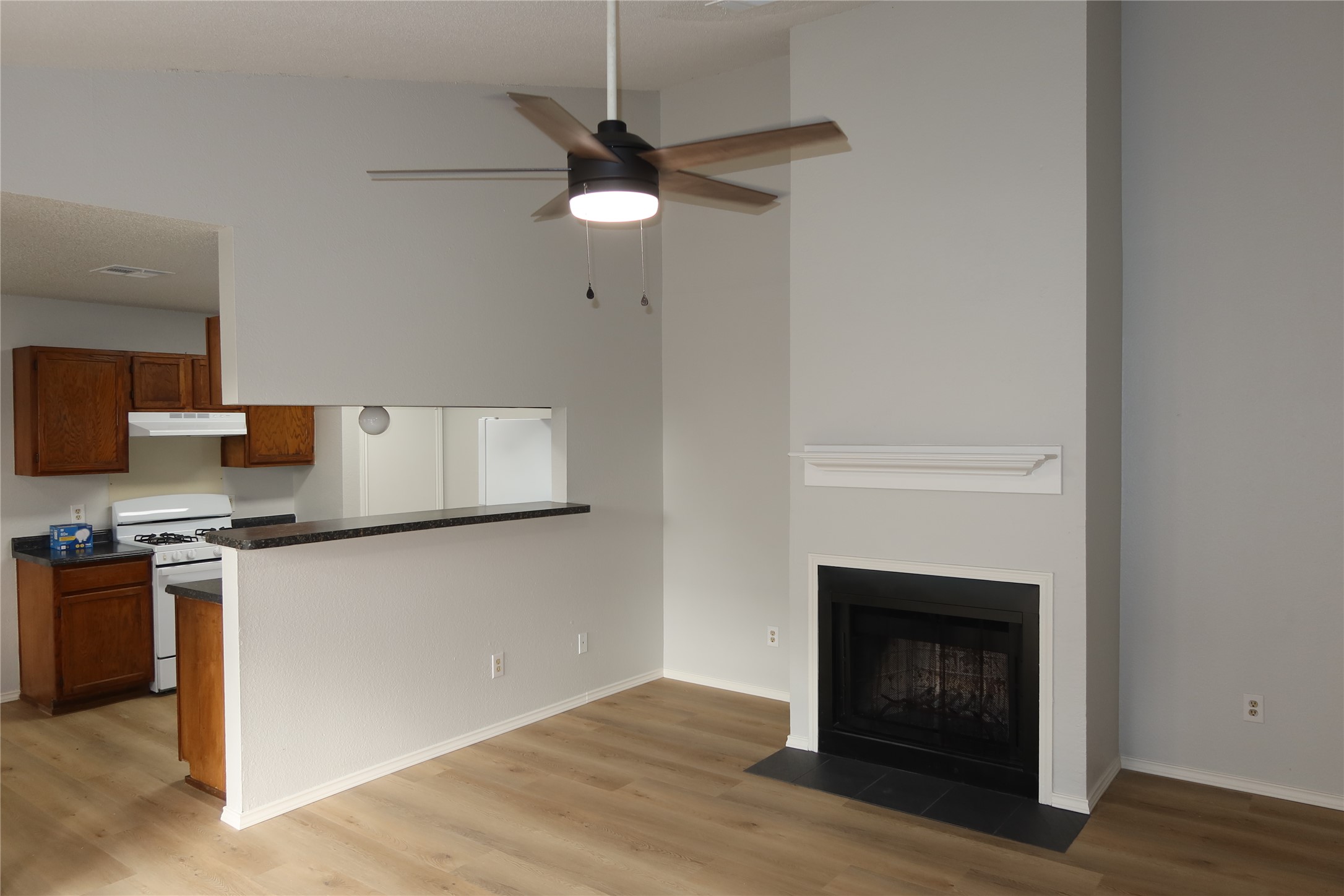 Unfurnished living room with a high ceiling, ceiling fan, light wood-style floors, and a fireplace with flush hearth