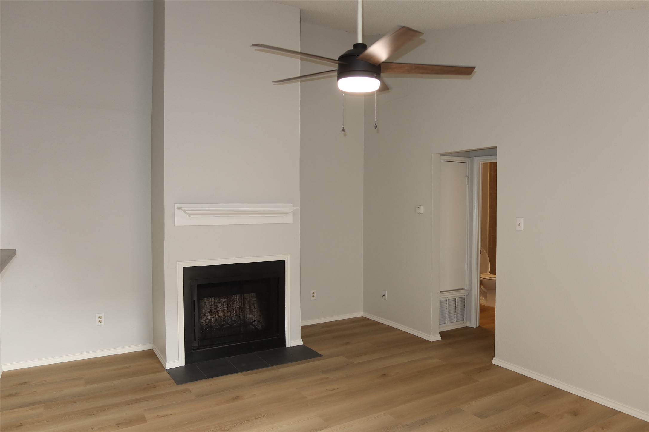 2511 Bucks Run, Unit A Austin, TX 78744 - Photo 2 of 25 Unfurnished living room featuring a high ceiling, wood finished floors, ceiling fan, and a fireplace with flush hearth