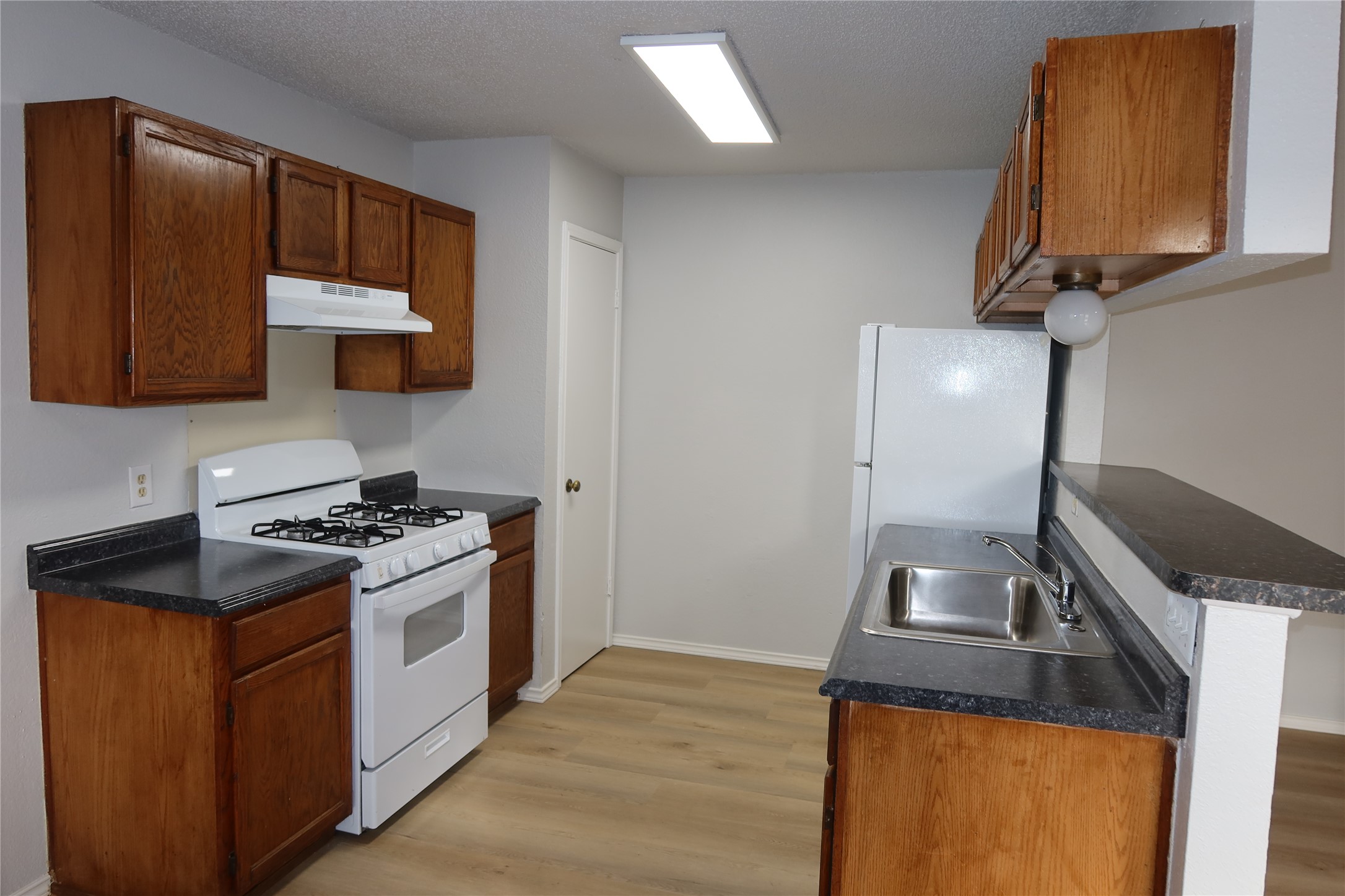 2511 Bucks Run, Unit A Austin, TX 78744 - Photo 5 of 25 Kitchen featuring dark countertops, white appliances, light wood finished floors, a peninsula, and a textured ceiling