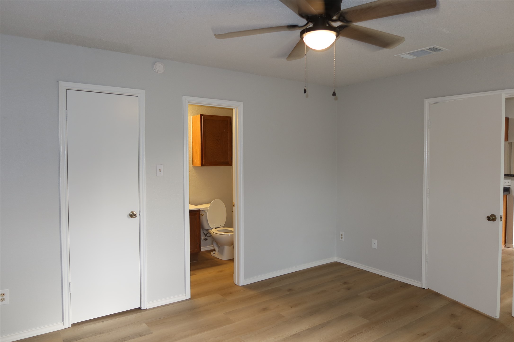 2511 Bucks Run, Unit A Austin, TX 78744 - Photo 10 of 25 Unfurnished bedroom with light wood-style flooring, connected bathroom, and ceiling fan