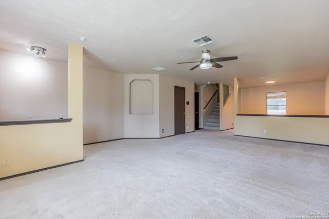 an empty room with chandelier fan and windows