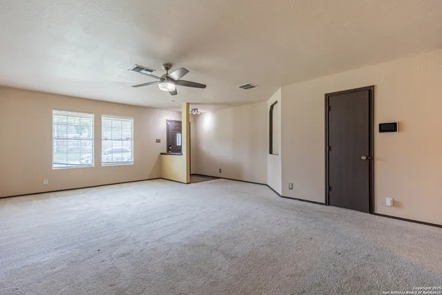an empty room with chandelier fan and windows