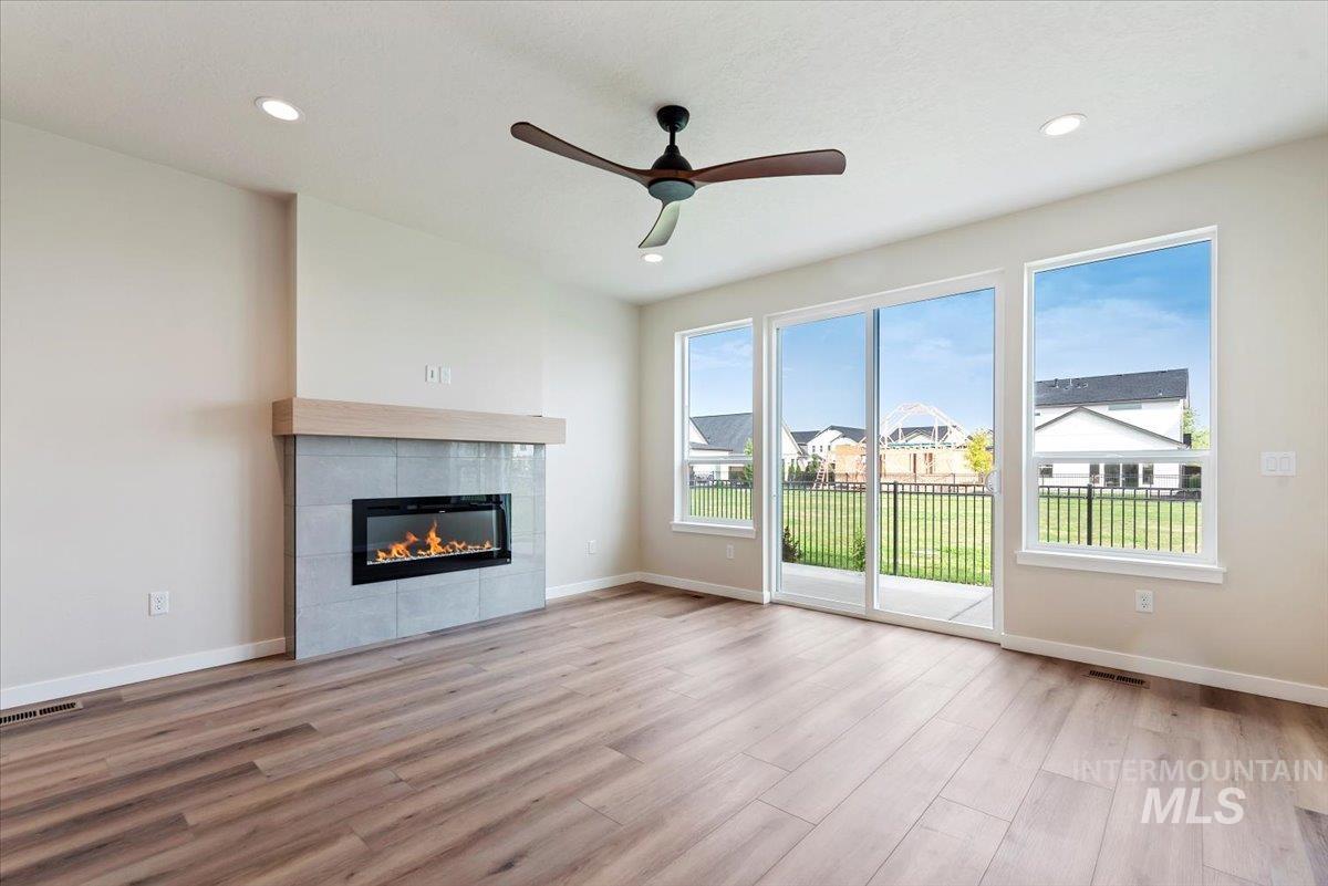 3866 West Spring House Lane Eagle, ID 83616 - Photo 7 of 33 Unfurnished living room featuring ceiling fan, light wood-style flooring, a tiled fireplace, recessed lighting, and a residential view