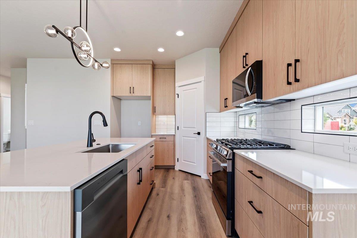 3866 West Spring House Lane Eagle, ID 83616 - Photo 9 of 33 Kitchen with light wood finished floors, stainless steel appliances, light stone countertops, light brown cabinets, and decorative light fixtures