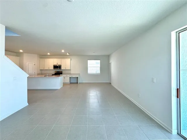 a view of an empty room and kitchen with window