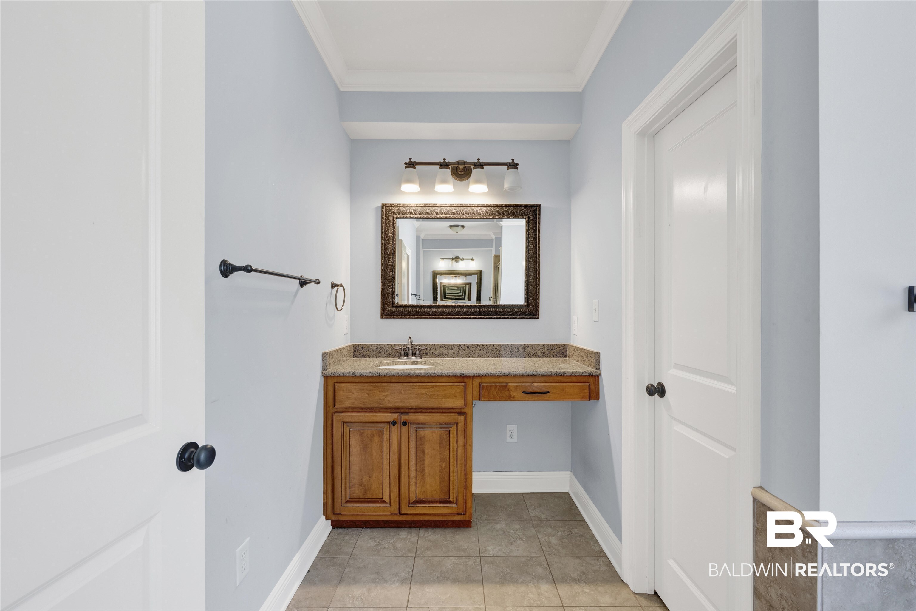 12944 Anna's Way Stapleton, AL 36578 - Photo 52 of 64 Vanity area featuring a granite-style countertop, integrated sink, wood-finish cabinetry, and a framed mirror with a three-light fixture
