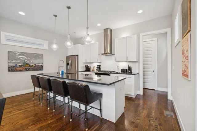 a kitchen with stainless steel appliances granite countertop a stove a sink a refrigerator a dining table and chairs with wooden floor