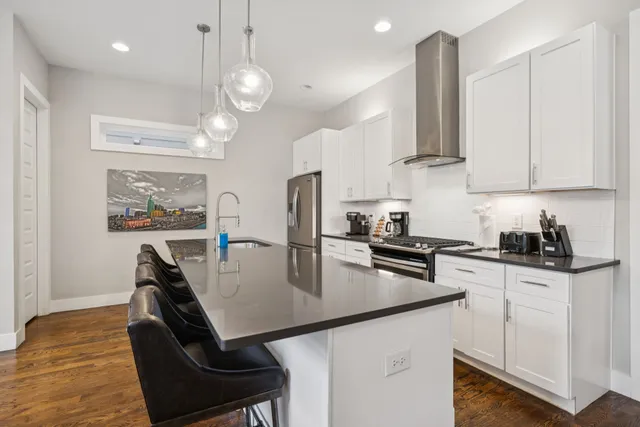 a kitchen with stainless steel appliances granite countertop a stove top oven a sink a dining table and chairs with wooden floor