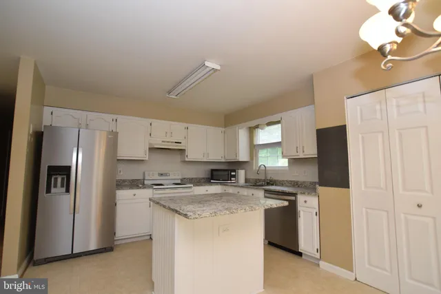 a kitchen with stainless steel appliances granite countertop a refrigerator a sink dishwasher a stove and white cabinets with wooden floor