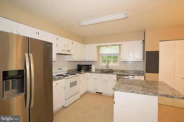 a kitchen with granite countertop a refrigerator sink stove and cabinets