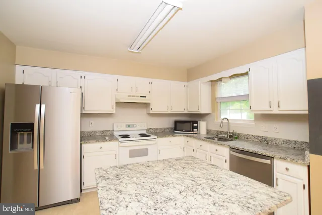 a kitchen with granite countertop a refrigerator sink stove and oven