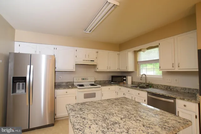 a kitchen with granite countertop a refrigerator sink stove and oven