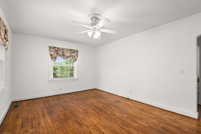 an empty room with wooden floor chandelier fan and windows