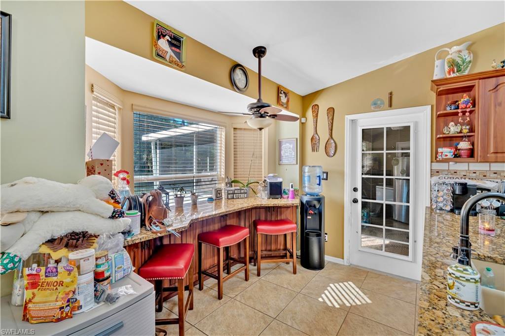 1867 17th Street Southwest Naples, FL 34117 - Photo 11 of 31 Kitchen with a kitchen breakfast bar, light tile patterned flooring, open shelves, ceiling fan, and light stone countertops