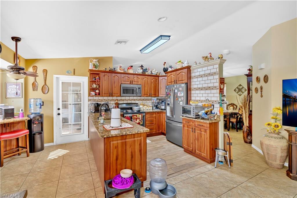 1867 17th Street Southwest Naples, FL 34117 - Photo 12 of 31 Kitchen with light stone counters, open shelves, stainless steel appliances, wood finish cabinetry, and lofted ceiling