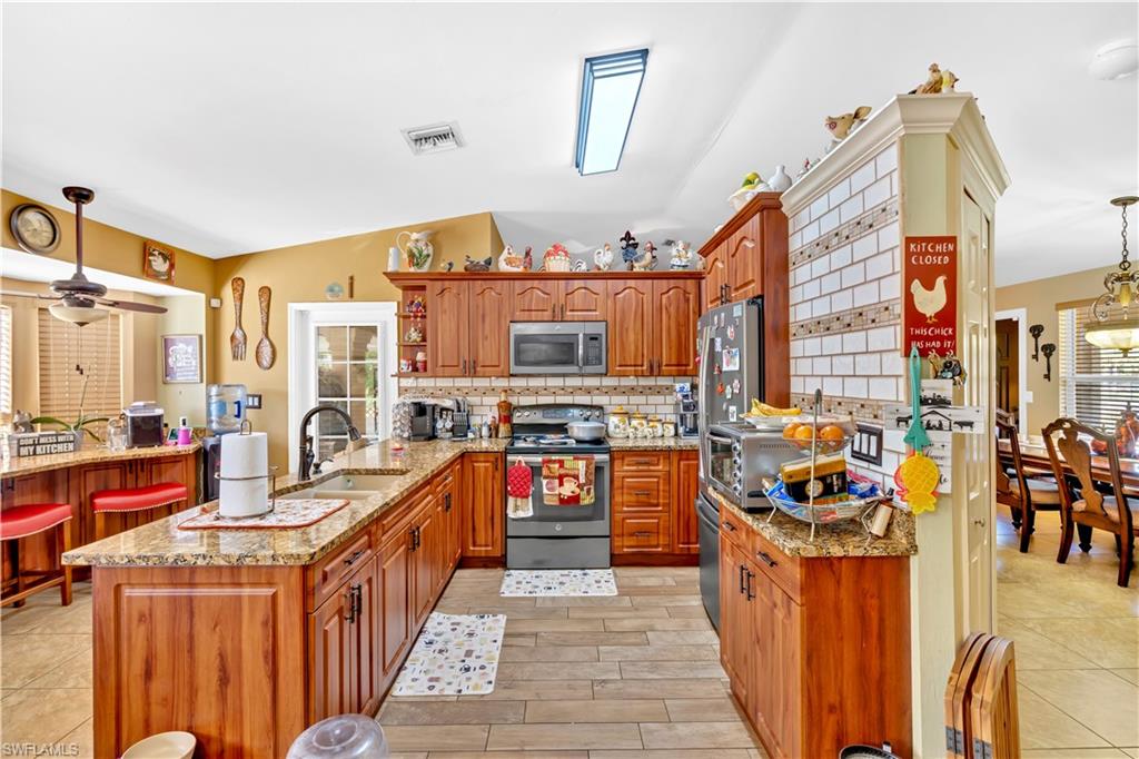 1867 17th Street Southwest Naples, FL 34117 - Photo 13 of 31 Kitchen featuring decorative light fixtures, stainless steel appliances, a peninsula, wood finish cabinets, and light stone countertops