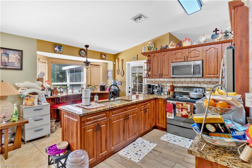 1867 17th Street Southwest Naples, FL 34117 - Photo 15 of 31 Kitchen featuring wood finish cabinets, stainless steel appliances, a peninsula, light stone countertops, and a ceiling fan